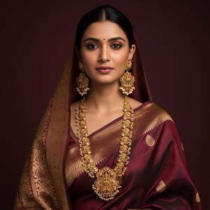 May include: A deep maroon silk saree with a gold brocade border, paired with an ornate gold long necklace featuring a central pendant and matching gold drop earrings. The jewelry is detailed with intricate metalwork and small white pearls.