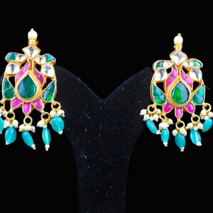 May include: A pair of gold earrings with green and pink gemstones. The earrings have a floral design with a teardrop-shaped center stone.