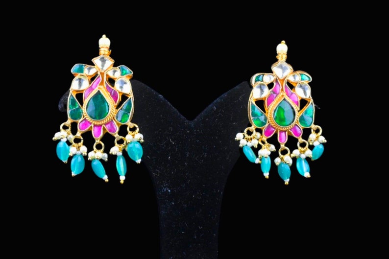 May include: A pair of gold earrings with green and pink gemstones. The earrings have a floral design with a teardrop-shaped center stone.