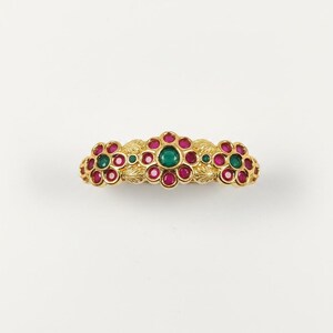 May include: A gold-toned barrette featuring a floral design with red and green gemstones. The barrette has a central row of gemstones and floral clusters on each end. The gemstones are set in a gold-colored metal.