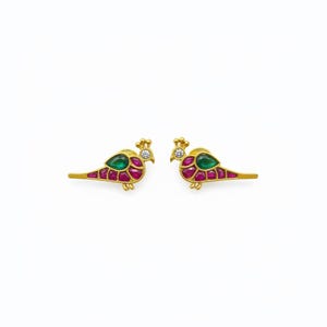 May include: A pair of gold peacock earrings. Each earring features a green emerald, red ruby, and a small diamond. The peacock's body is adorned with red and gold accents. The earrings are set against a white background.