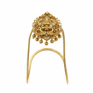 May include: A gold-colored headpiece with an ornate design. The central element features a seated figure, surrounded by intricate patterns, small gems, and dangling spheres. Two long, braided chains extend downwards, creating a U-shape.