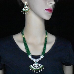 Puede incluir: Un collar de cuentas verdes y blancas con un juego de pendientes a juego. El collar presenta un gran colgante adornado con un diseño en forma de abanico.