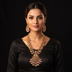 May include: A gold-toned necklace and matching earrings set. The necklace features intricate detailing with red and white accents. The earrings have a similar design. The jewelry is worn against a black background.