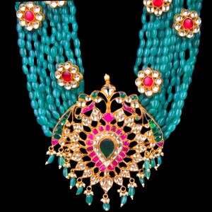 May include: A multi-strand necklace with a large, ornate pendant. The necklace is made of green beads and the pendant is gold with red, pink, and green gemstones.