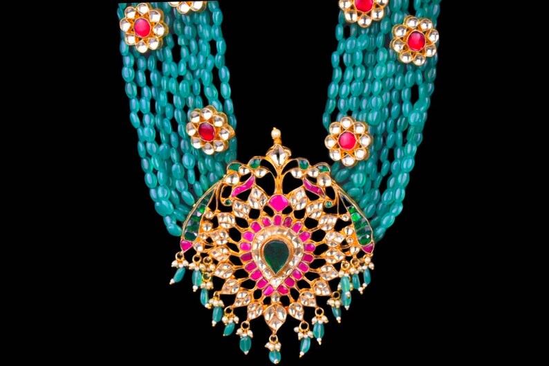 May include: A multi-strand necklace with a large, ornate pendant. The necklace is made of green beads and the pendant is gold with red, pink, and green gemstones.
