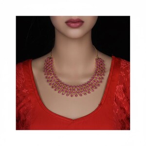 May include: A gold-toned necklace featuring a wide, semi-circular collar design composed of multiple rows of small, vibrant pink circular stones arranged in a repeating lattice pattern, secured by thin gold chains on each side of the neck.