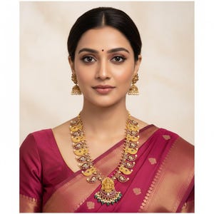 May include: A gold-toned necklace and matching jhumka earrings set featuring intricate paisley-shaped motifs with embedded red and green stones. The central pendant displays a detailed deity figure with dangling green and white beads.