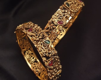 May include: Two gold bangles with intricate peacock designs and red and green gemstones.