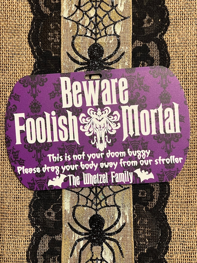 May include: Purple and black Halloween sign with the text "Beware Foolish Mortal" and "This is not your doom buggy. Please drag your body away from our stroller. The Whetzel Family."