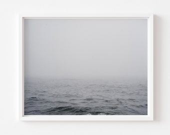 May include: A framed photograph of a foggy ocean scene. The water is a dark gray and the fog is a light gray. The horizon is barely visible.