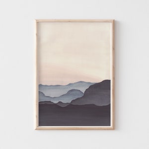 May include: A framed watercolor print featuring a minimalist landscape. The artwork depicts layered mountain silhouettes in shades of blue and gray against a soft, peachy sky. The frame is a light wood color, adding a natural touch to the artwork.