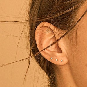 Puede incluir: Primer plano de la oreja de una persona con cuatro pequeños pendientes de diamantes.