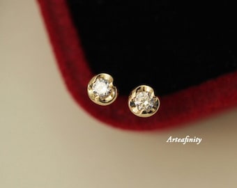 May include: A pair of small gold stud earrings with a single clear diamond in each earring.