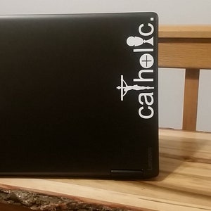 May include: A black laptop with a white sticker that says "catholic" with a chalice and a crucifix.