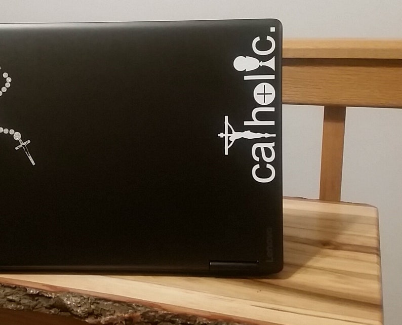 May include: A black laptop with a white sticker that says "catholic" with a chalice and a crucifix.