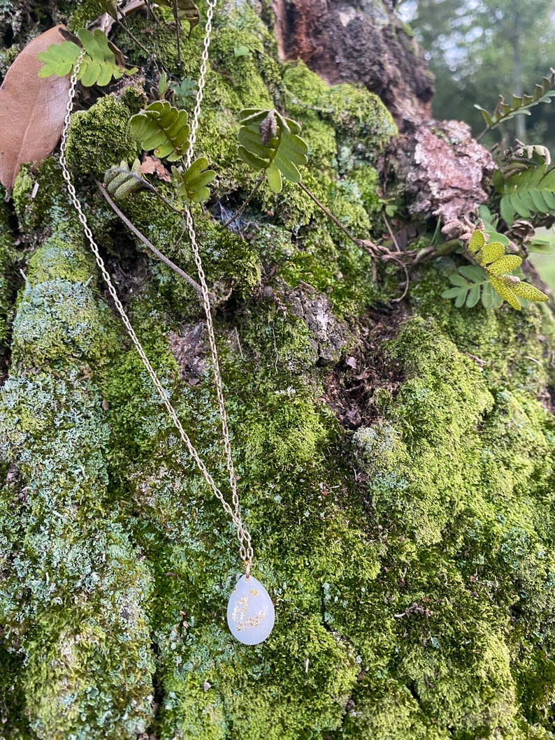 Puede incluir: Un collar de cadena plateada con un colgante blanco en forma de l&aacute;grima con un dise&ntilde;o de media luna dorada y estrellas.