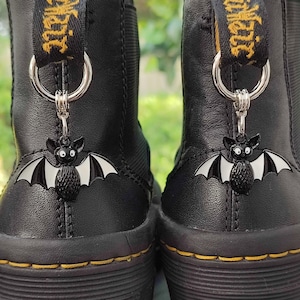 May include: A pair of black leather boots with a yellow and black ribbon and a black bat charm attached to each boot.