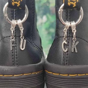 May include: A pair of black leather boots with silver charms spelling out "F U C K" hanging from the laces.