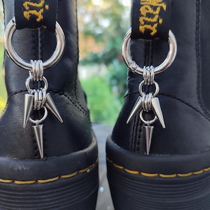 May include: A pair of black leather boots with silver zipper pulls. The zipper pulls have a silver ring with a silver spike charm attached.