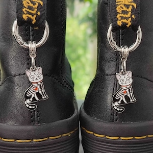 May include: A pair of black leather boots with a skeleton cat charm attached to the zipper pull. The charm is silver with white details and a red heart.