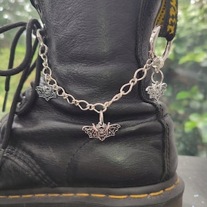 May include: A black leather boot with a silver chain and three bat charms attached. The chain is attached to a silver ring on the boot.