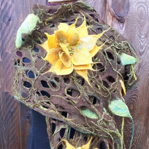 Puede incluir: Una chal de fieltro marrón y verde con detalles de flores amarillas. La chal tiene un diseño de encaje, calado y está drapeado sobre un vestido negro.