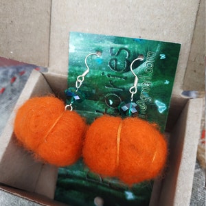 May include: A pair of orange felt pumpkin earrings with green crystal accents. The earrings are hanging from silver hooks.