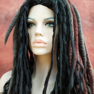 May include: A black and grey dreadlock wig with a few strands of burgundy wool. The wig is styled in a long, flowing style.