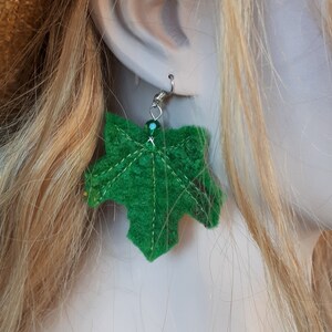 Puede incluir: Pendientes de hoja de fieltro verde con gancho plateado y una cuenta de cristal verde.