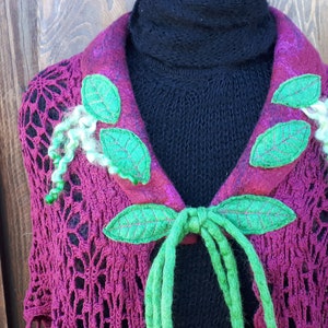 May include: A burgundy crocheted shawl with green felt leaves and green felt ties. The shawl has a high collar and is decorated with green felt leaves.