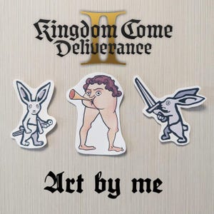 Può includere: Un set di adesivi con personaggi e testo da "Kingdom Come: Deliverance 2". Gli adesivi includono una figura che suona una tromba, due conigli con spade e la frase "Art by me".