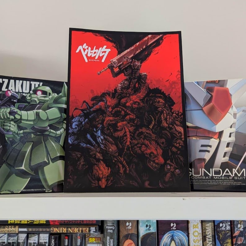 May include: A poster featuring a character with a large sword, set against a red background. The artwork depicts a figure atop a mass of grotesque creatures. The Japanese text is visible at the top. Other posters are visible on either side.