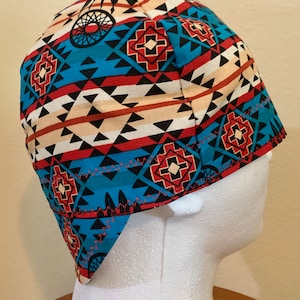 May include: A patterned cap featuring a Native American-inspired design. The cap showcases a vibrant mix of colors, including turquoise, red, black, and beige, with geometric and dreamcatcher motifs. The cap is designed to fit snugly on the head.