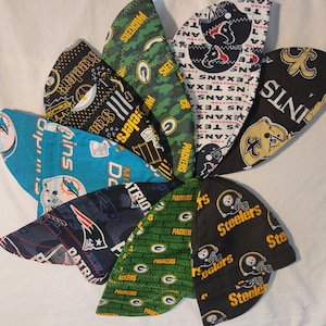 May include: A collection of football team-themed head wraps, featuring logos and colors of the Steelers, Packers, Patriots, Saints, and Texans. The head wraps are made of fabric and are arranged in a circular pattern.
