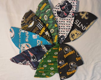 May include: A collection of football team-themed head wraps, featuring logos and colors of the Steelers, Packers, Patriots, Saints, and Texans. The head wraps are made of fabric and are arranged in a circular pattern.