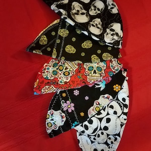 May include: Five fabric face masks with different skull and sugar skull designs. The masks are black, white, red, and yellow.