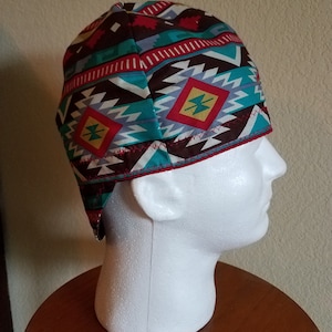 May include: A patterned cap with a Southwestern design. The cap features a repeating geometric pattern in shades of brown, teal, red, and gray. The cap is worn on a white mannequin head, showcasing the design and fit.