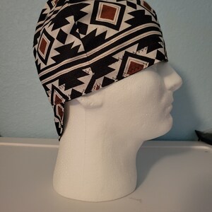 May include: A black, white, and brown patterned welding cap. The cap features a geometric design with brown squares and zig-zag shapes. The cap is made of fabric and is designed to protect the head and hair.