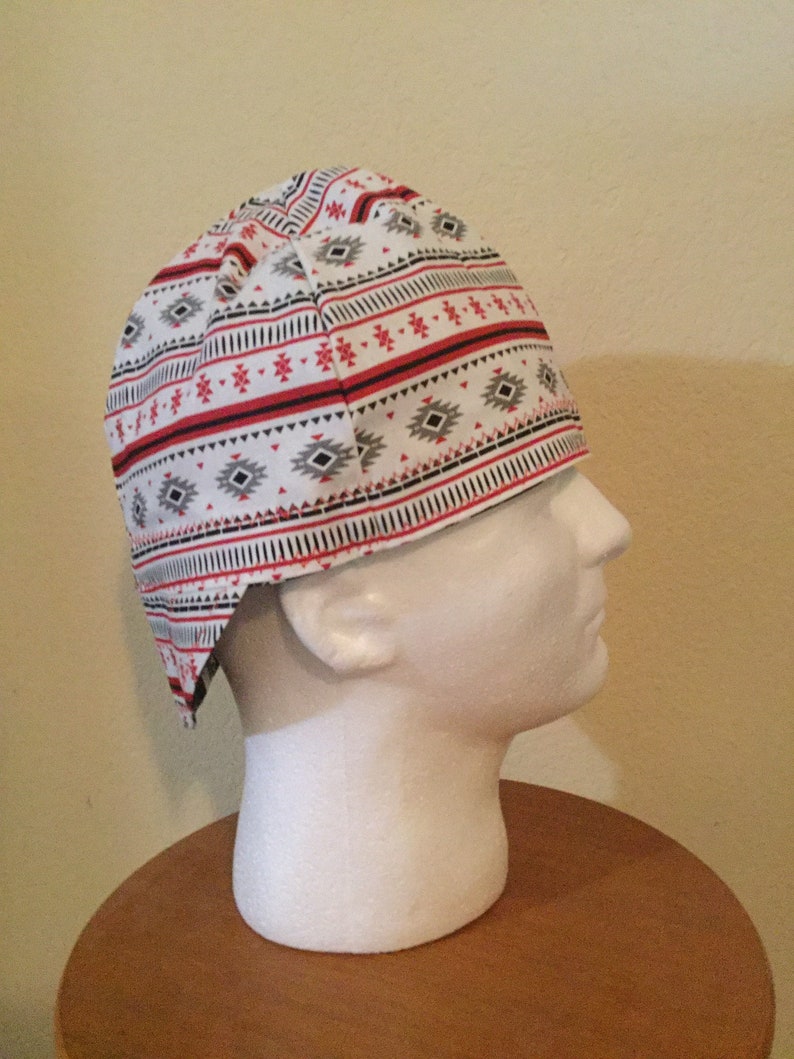 May include: A white head wrap with a geometric pattern in red, black, and gray. The fabric features horizontal stripes and diamond shapes, creating a Southwestern or Native American inspired design. The head covering is displayed on a white mannequin head.