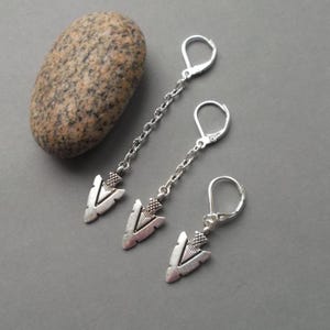 May include: A set of three silver arrowhead earrings with a chain dangle. The earrings are on a gray background.