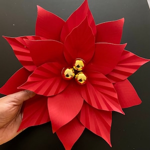 May include: A red paper poinsettia flower with three gold ornaments in the center.