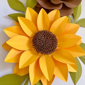 May include: A large paper sunflower with yellow petals and a brown center. The sunflower is surrounded by green leaves.