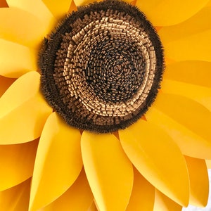 May include: A large paper sunflower with yellow petals and a brown center. The center is made of many small, layered pieces of paper.
