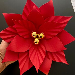May include: A red paper poinsettia flower with gold glitter ornaments in the center.