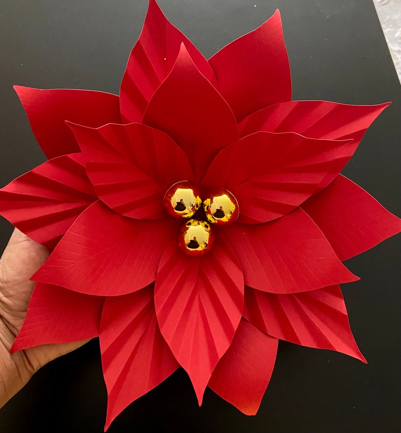 May include: A red paper poinsettia flower with gold glitter ornaments in the center.