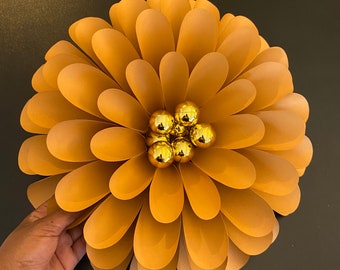 May include: A large, brown paper flower with a center made of gold-colored ornaments. The flower is made of many overlapping petals.