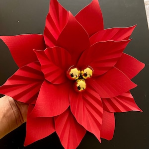 May include: A red paper poinsettia flower with gold glitter ornaments in the center.