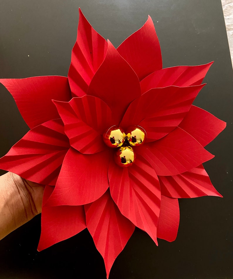May include: A red paper poinsettia flower with gold glitter ornaments in the center.
