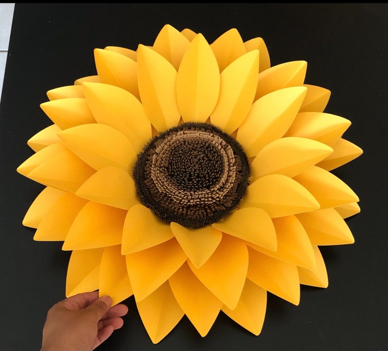 May include: A large, paper sunflower with yellow petals and a brown center. The sunflower is made of multiple layers of paper petals.
